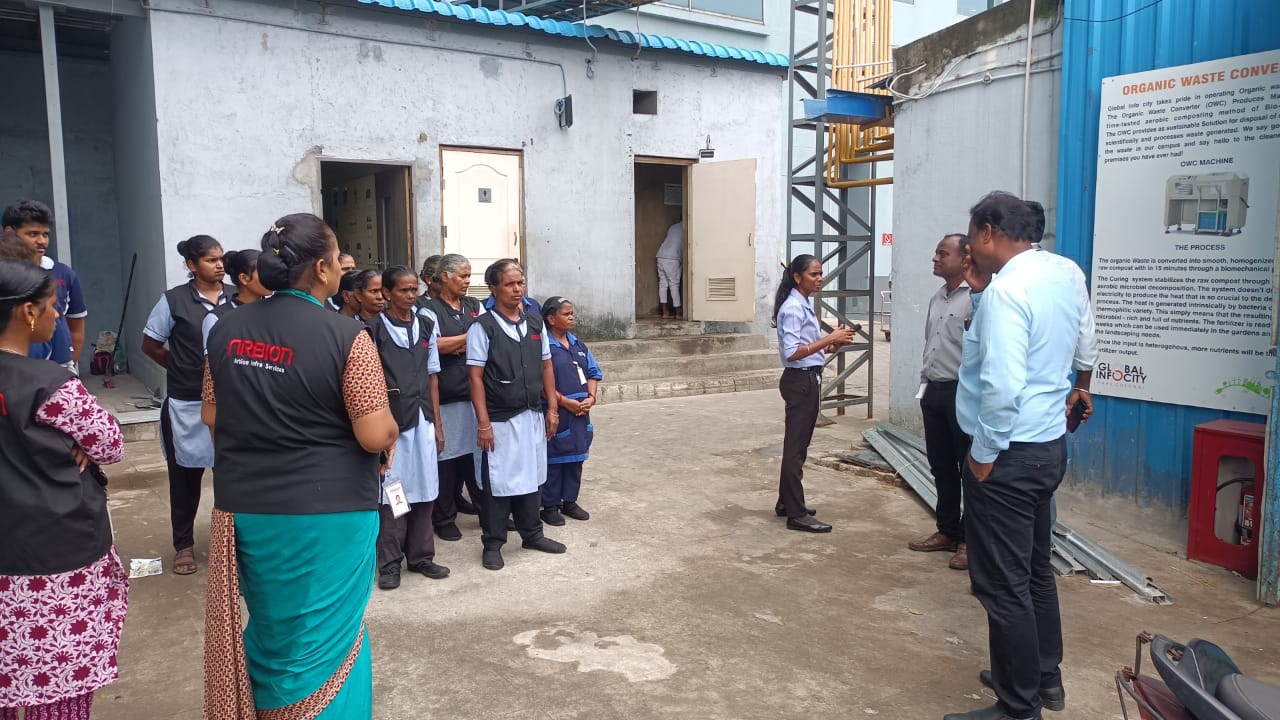 Team briefing beside organic waste converter signage